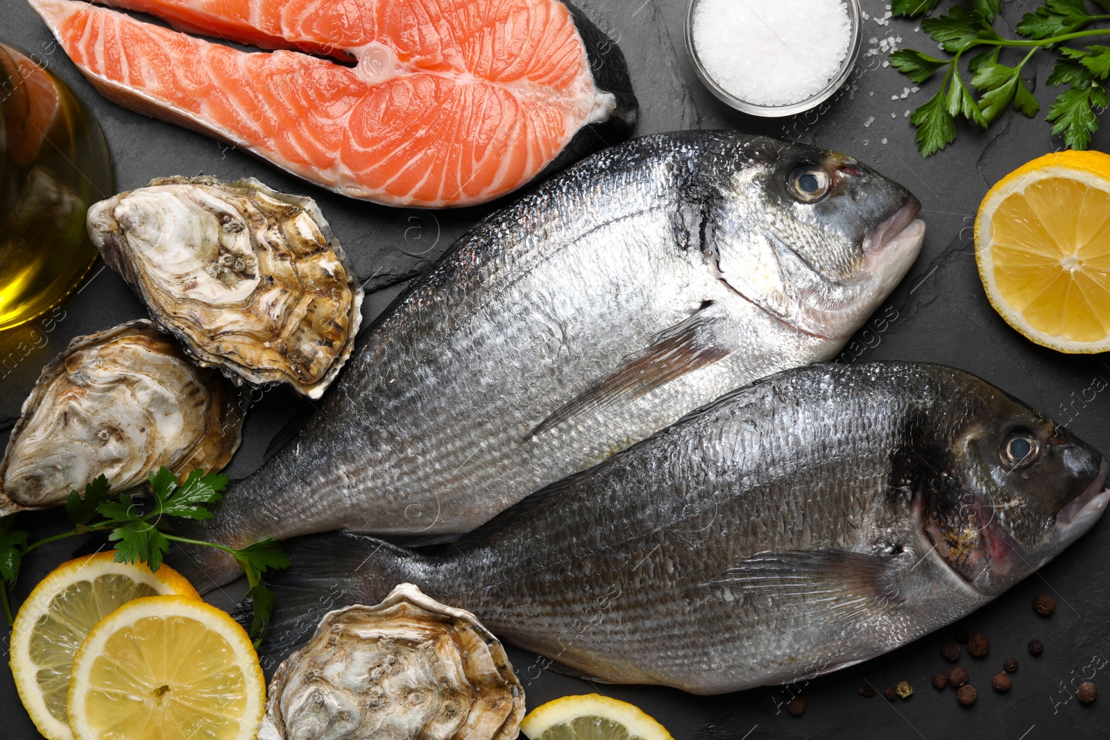 Photo of Fresh dorado fish and other seafood on black slate background, flat lay