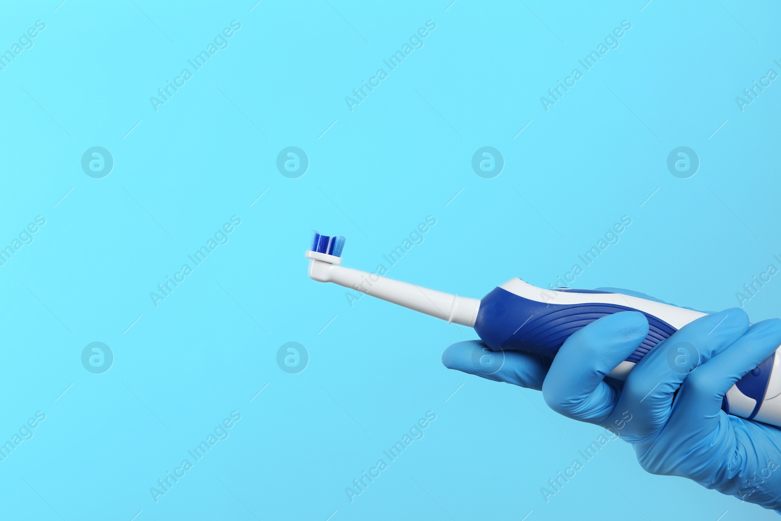 Photo of Dentist holding electric toothbrush on color background, space for text