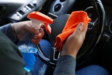 Photo of Man cleaning steering wheel with rag and spray bottle in car, closeup