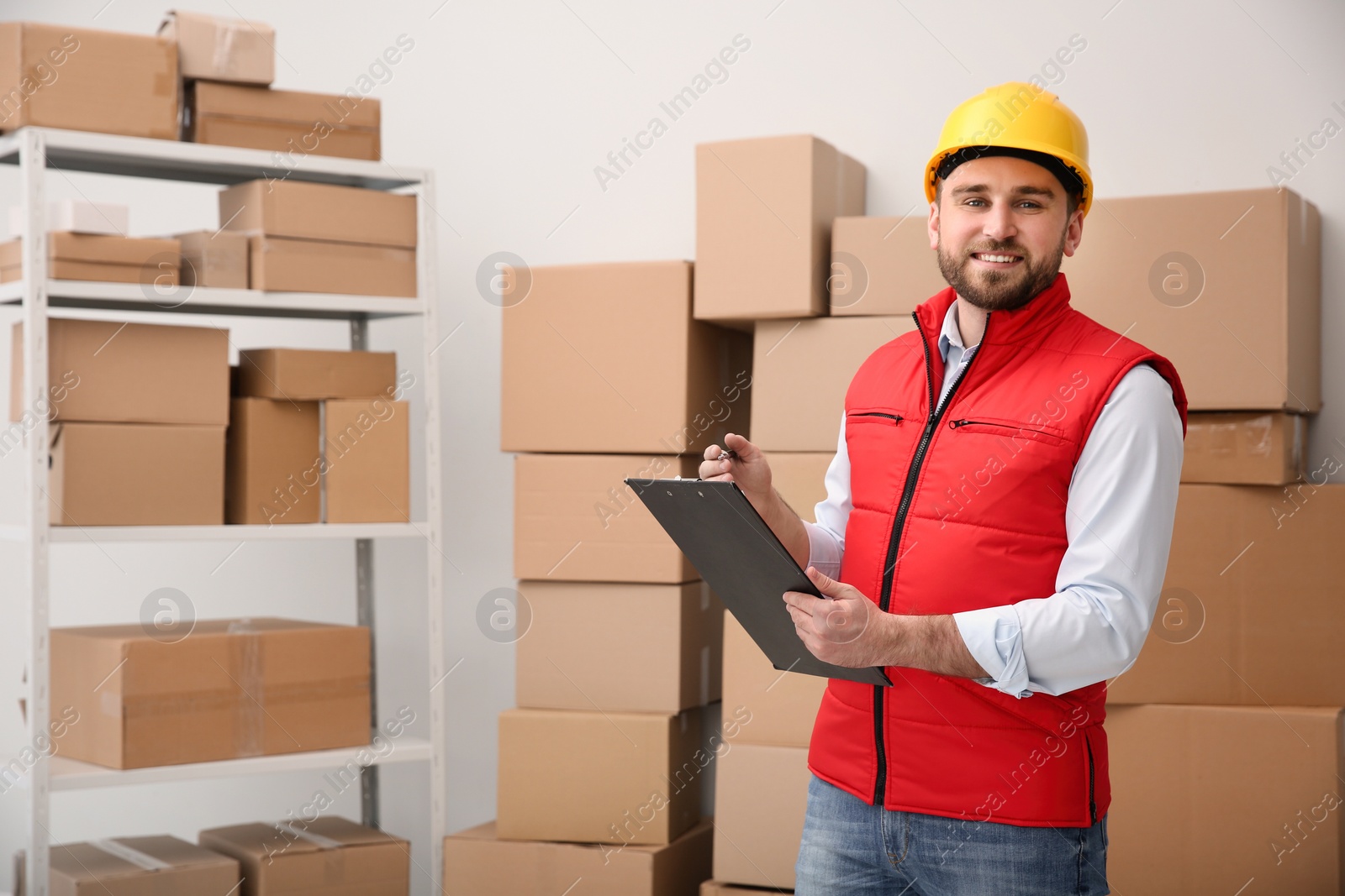 Photo of Young man with clipboard near cardboard boxes at warehouse