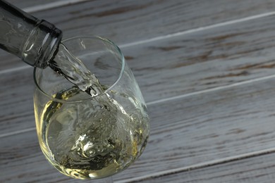 Photo of Pouring tasty aromatic wine in glass at wooden table, closeup. Space for text