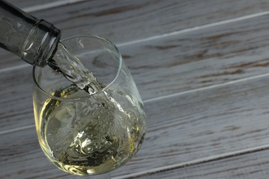 Pouring tasty aromatic wine in glass at wooden table, closeup. Space for text