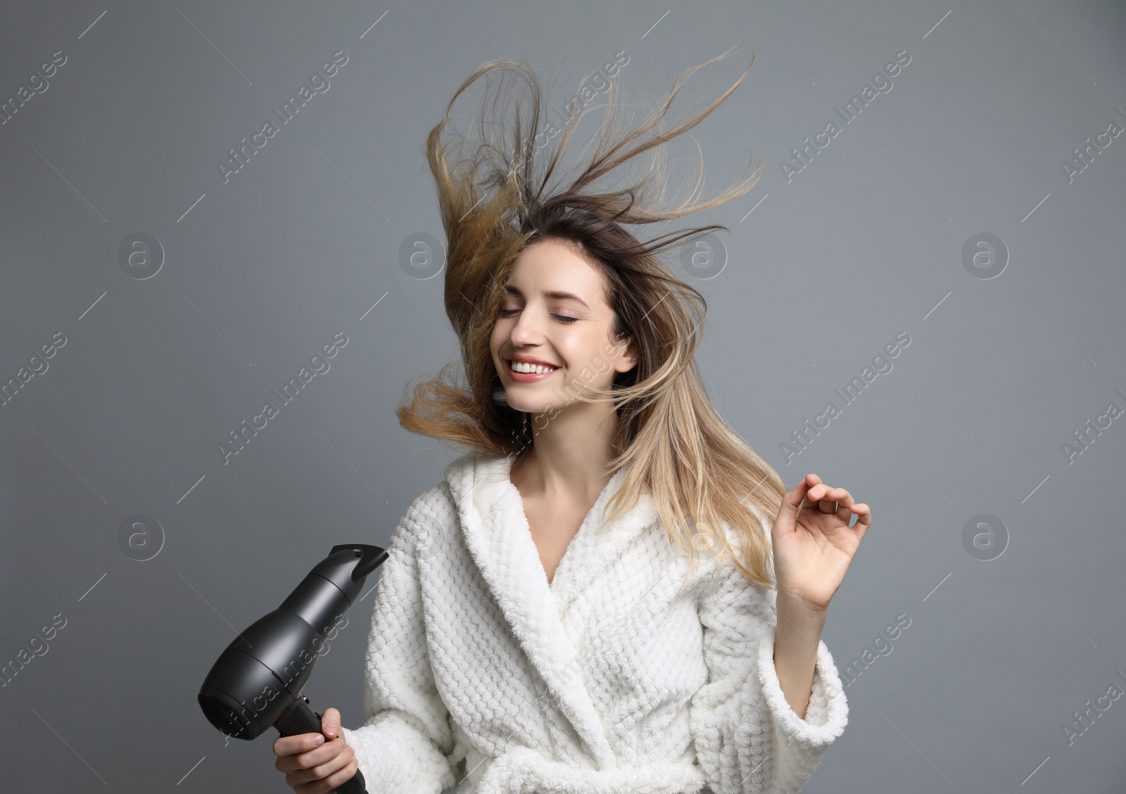 Photo of Beautiful young woman using hair dryer on grey background