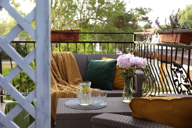 Photo of Rattan table with jug of water, glasses and beautiful flowers on terrace