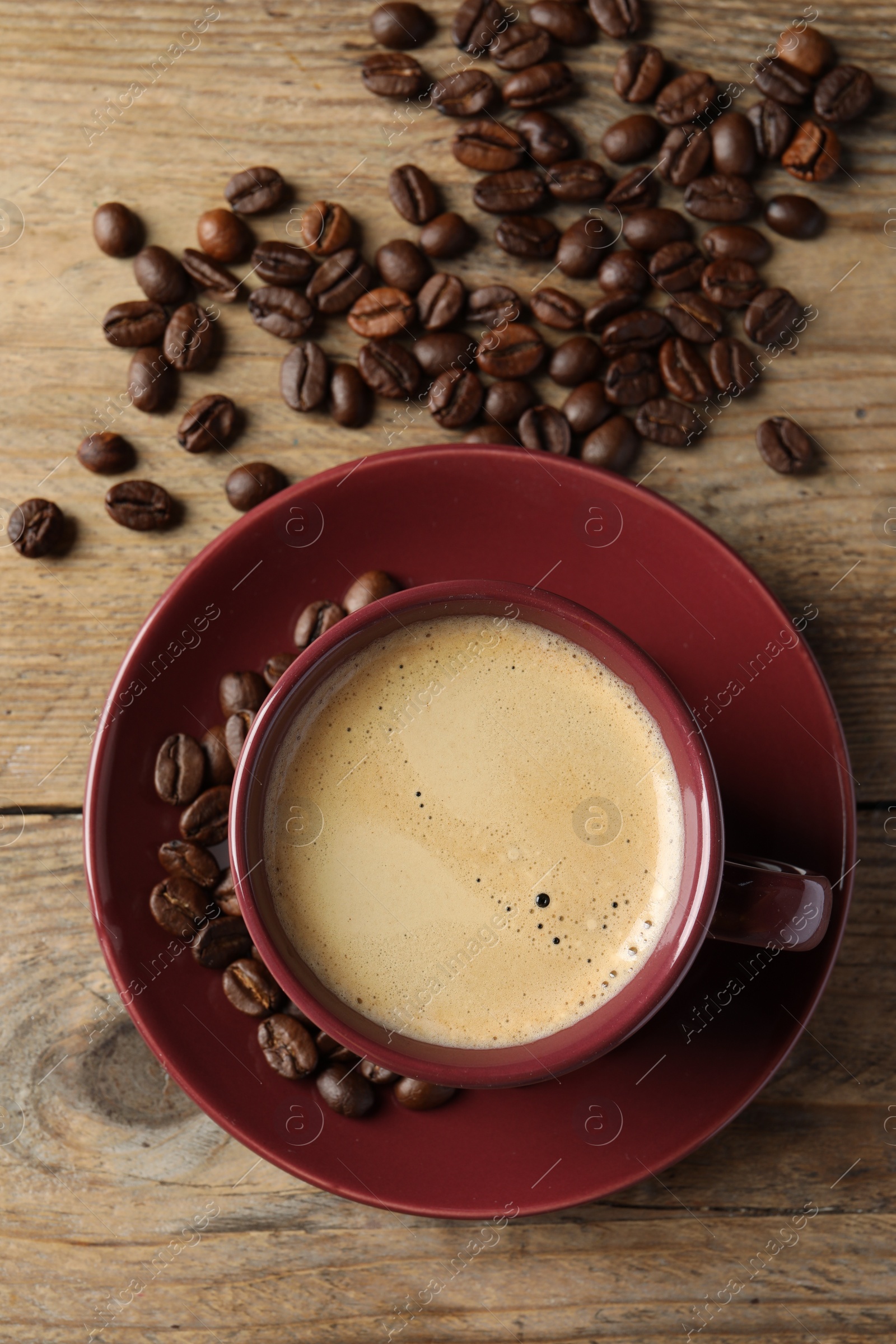 Photo of Cup of hot aromatic coffee and roasted beans on wooden table, flat lay