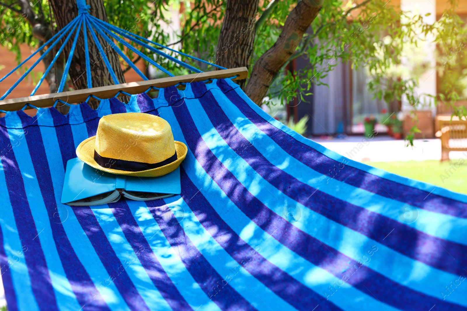 Photo of Comfortable blue hammock with hat and book outdoors on sunny day