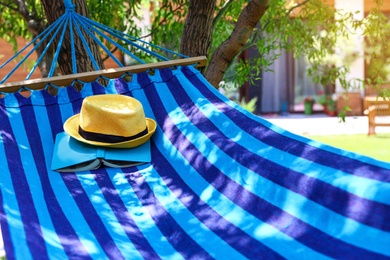 Photo of Comfortable blue hammock with hat and book outdoors on sunny day