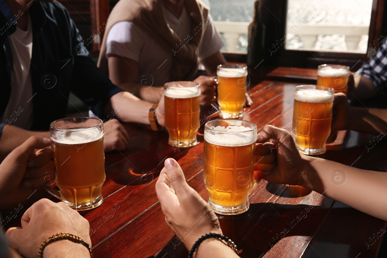 Photo of Friends with tasty beer at wooden table in pub, closeup