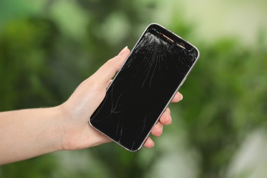 Photo of Woman holding damaged smartphone on blurred green background, closeup. Device repairing