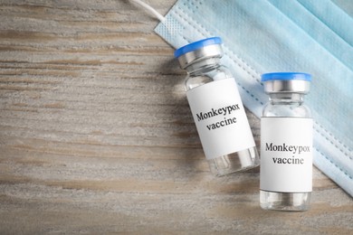 Monkeypox vaccine in glass vials and medical mask on wooden table, flat lay. Space for text