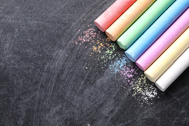 Photo of Pieces of color chalk on blackboard, flat lay. Space for text