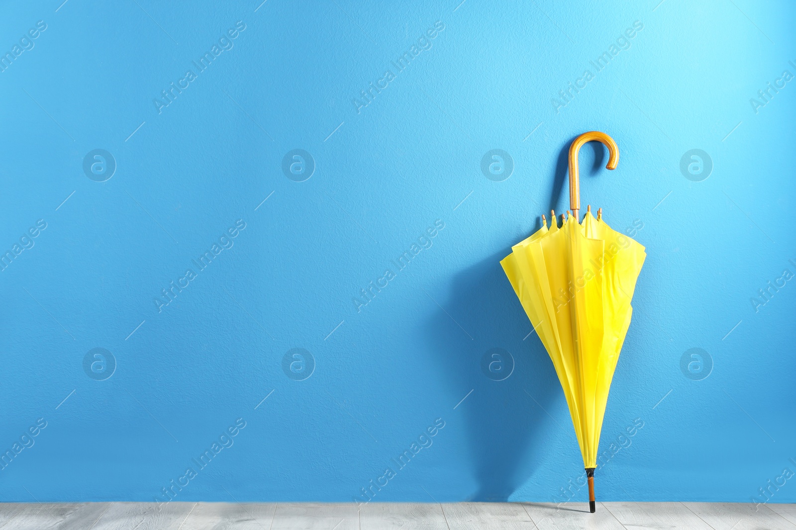 Photo of Beautiful yellow umbrella near blue wall. Space for text