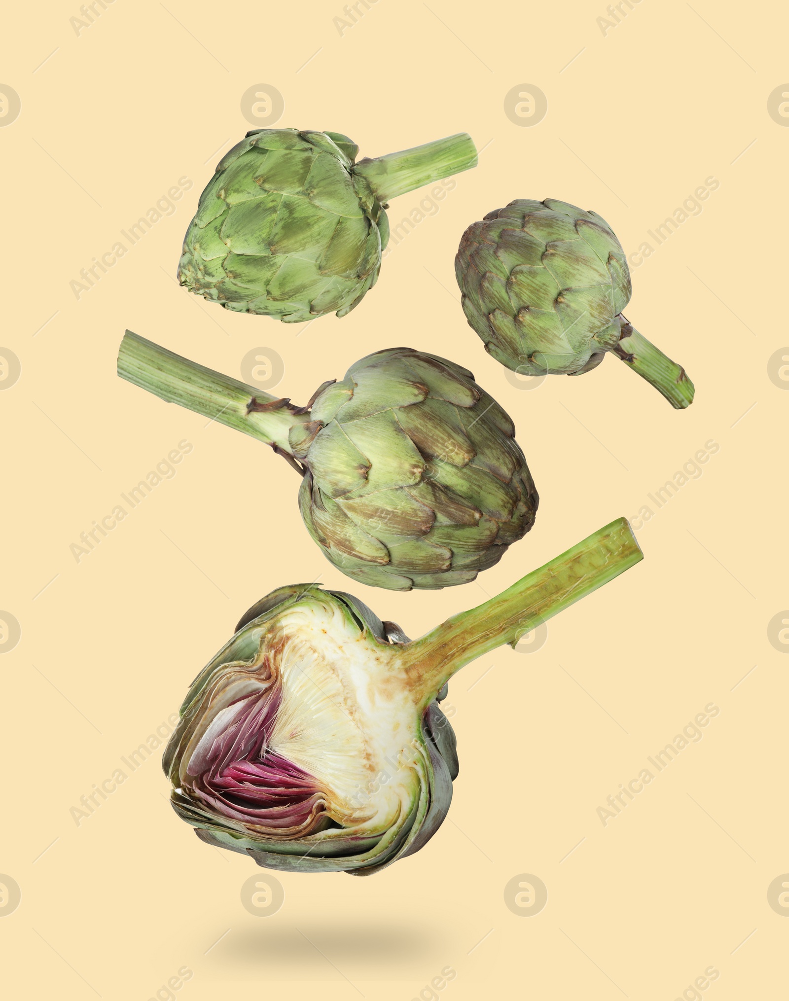 Image of Fresh raw artichokes falling on pale yellow background