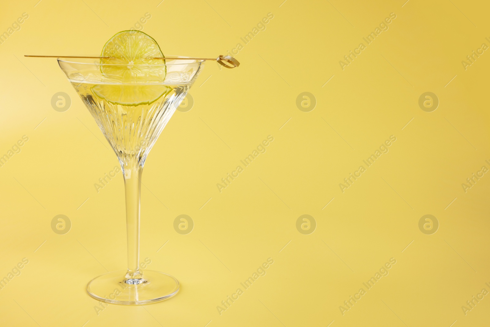 Photo of Martini cocktail with lime slice on yellow background, space for text