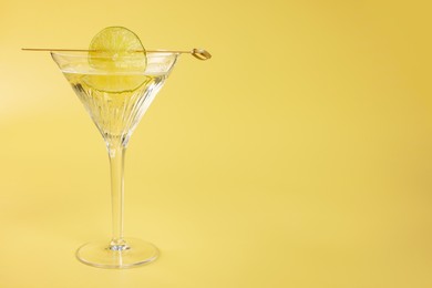 Martini cocktail with lime slice on yellow background, space for text