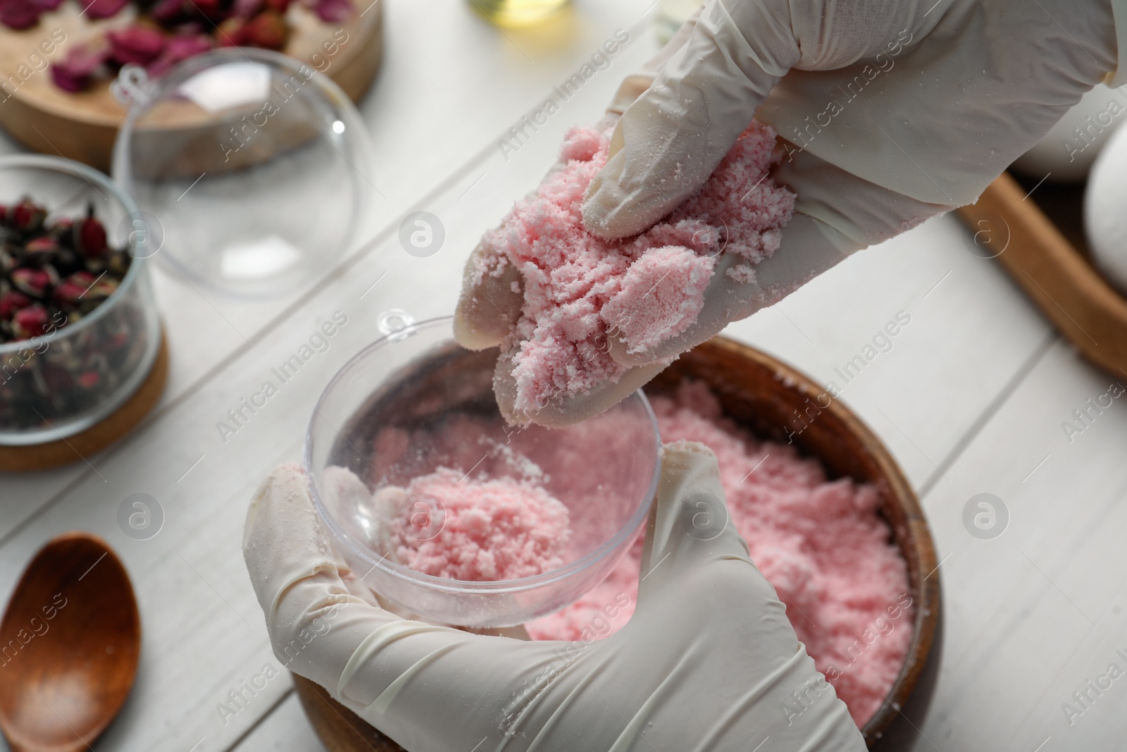 Photo of Woman in gloves making bath bomb at white table, closeup