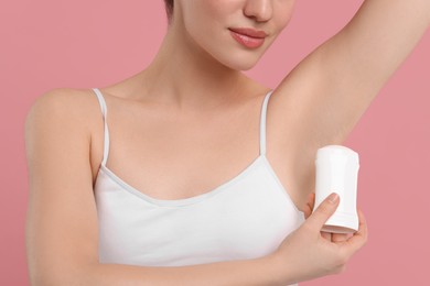Photo of Woman applying deodorant on pink background, closeup