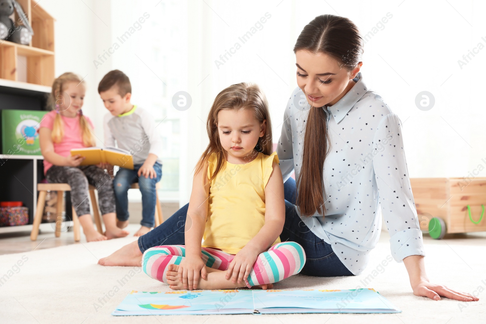 Photo of Kindergarten teacher reading book to child indoors. Learning and playing