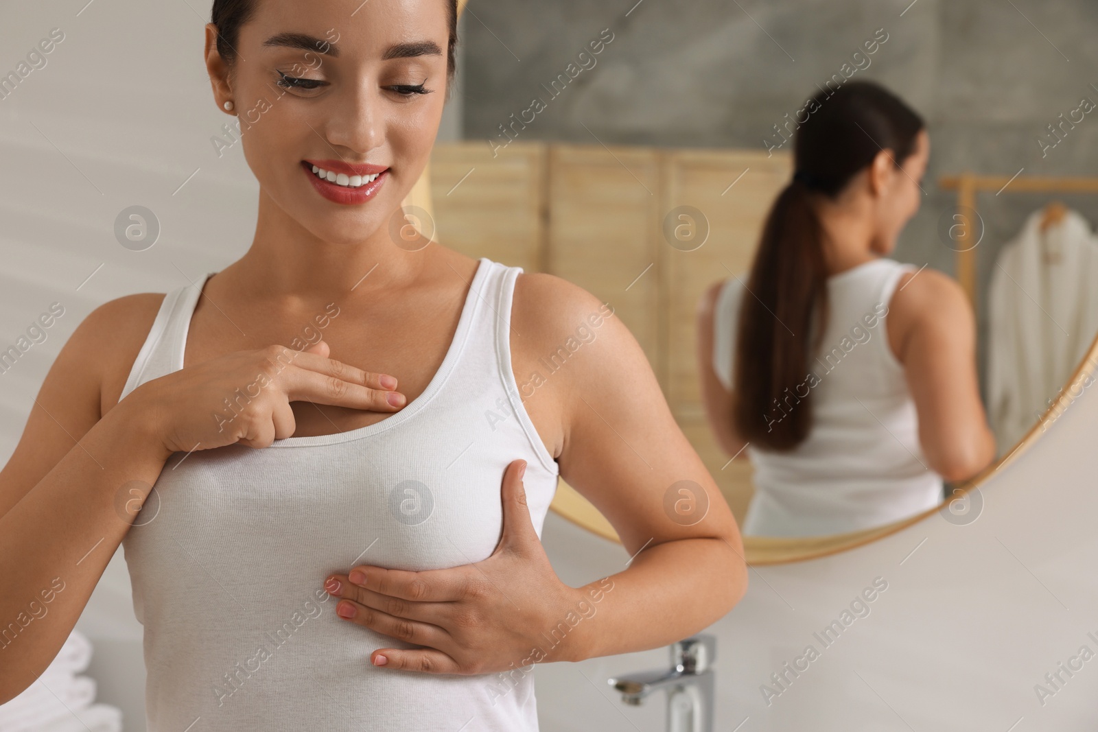 Photo of Beautiful young woman doing breast self-examination in bathroom, space for text