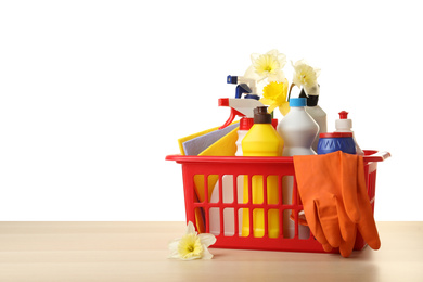 Photo of Basket with spring flowers and cleaning supplies on wooden table. Space for text