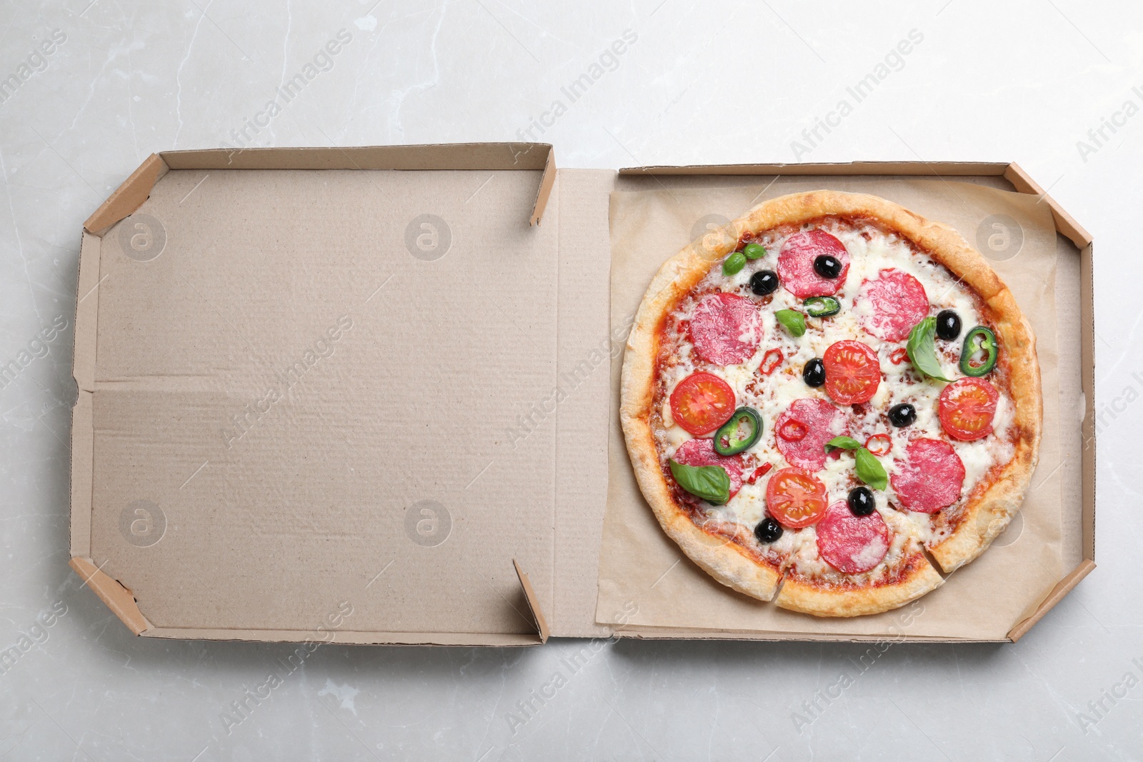 Photo of Delicious pizza Diablo in cardboard box on light marble background, top view