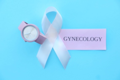 Flat lay composition with symbolic ribbon of breast cancer awareness and wristwatch on color background. Gynecological care