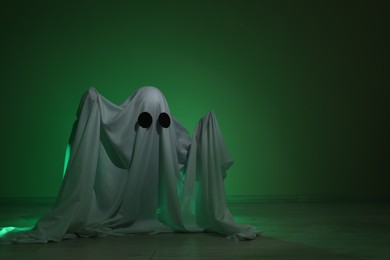 Creepy ghost. Woman covered with sheet in green light, space for text