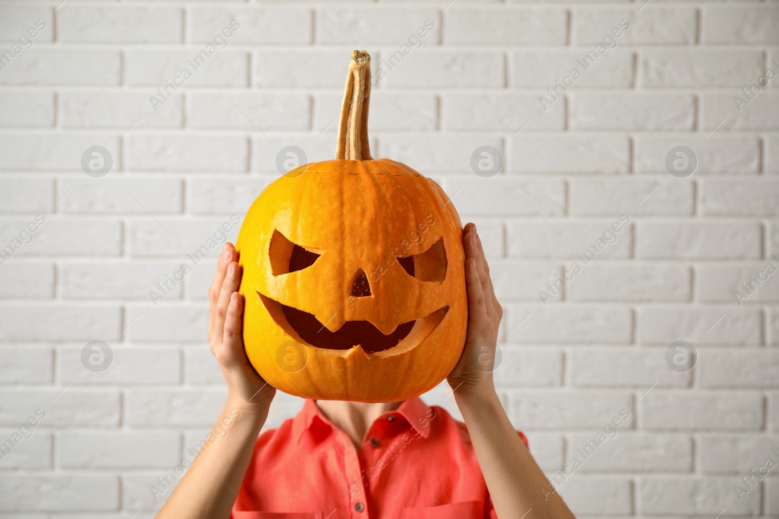 Photo of Woman with pumpkin head near white brick wall. Jack lantern - traditional Halloween decor
