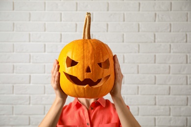 Photo of Woman with pumpkin head near white brick wall. Jack lantern - traditional Halloween decor