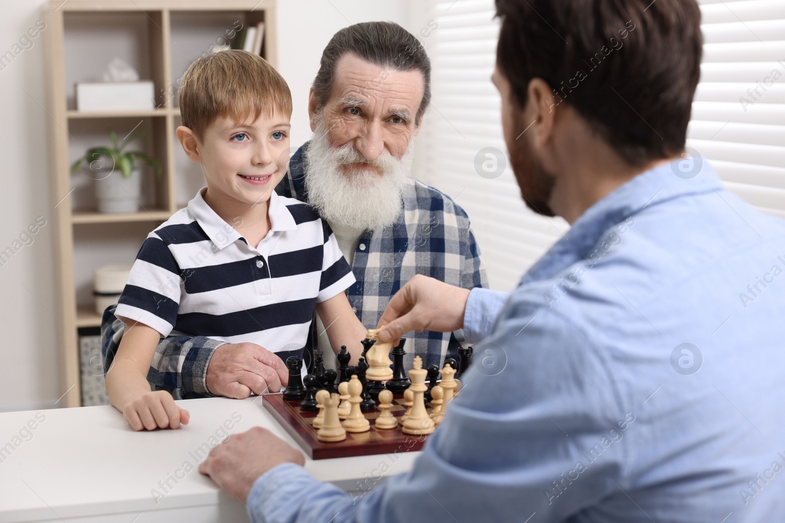 Photo of Family playing chess together at table in room