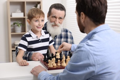 Photo of Family playing chess together at table in room