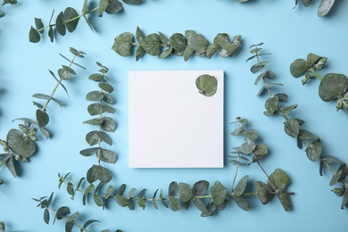 Fresh eucalyptus leaves and blank card with space for design on color background, top view