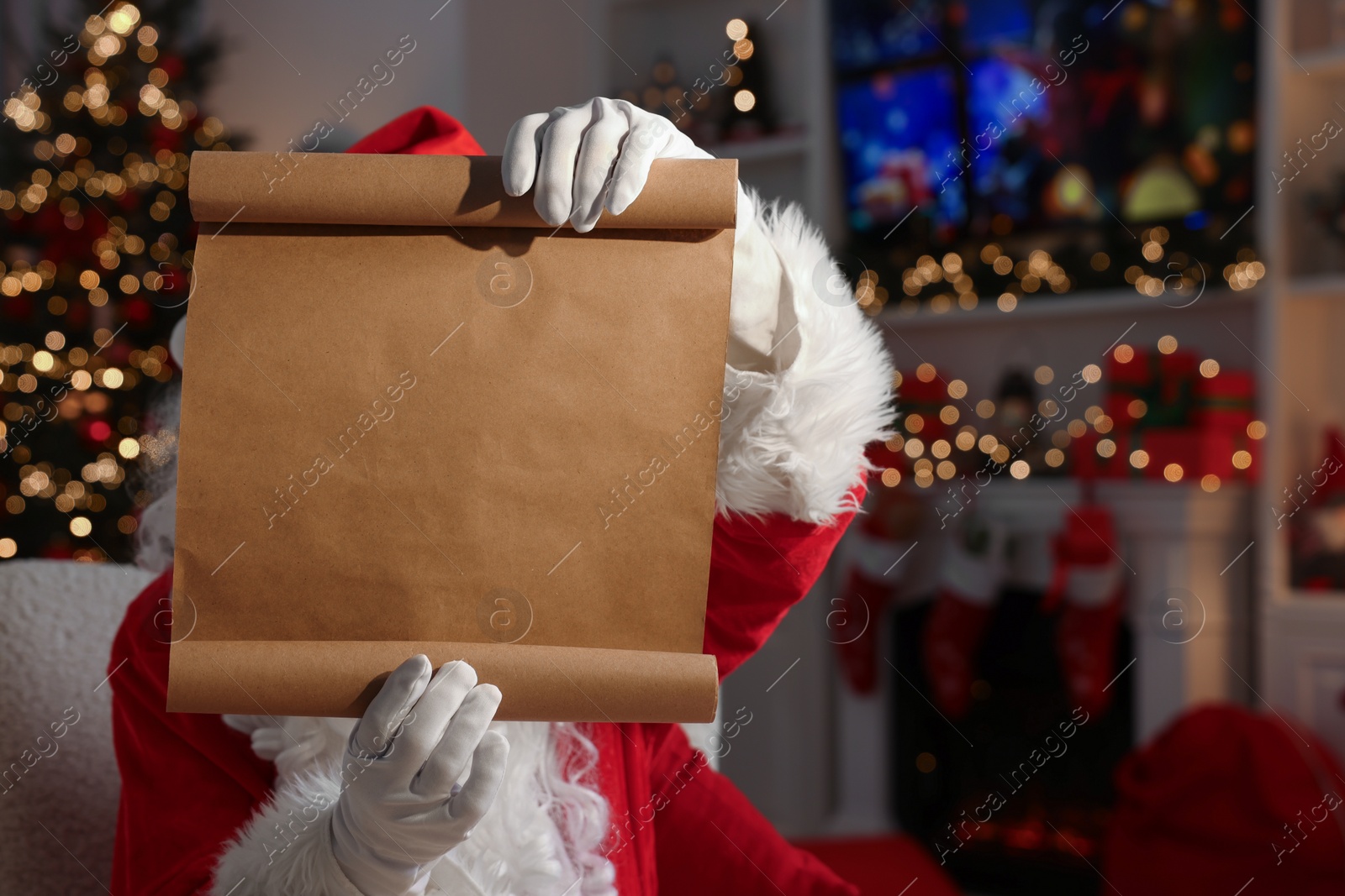 Photo of Merry Christmas. Santa Claus showing blank paper sheet at table in room, space for text