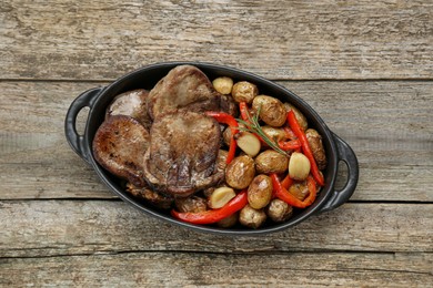 Tasty beef tongue pieces with potatoes, pepper and rosemary on wooden table, top view