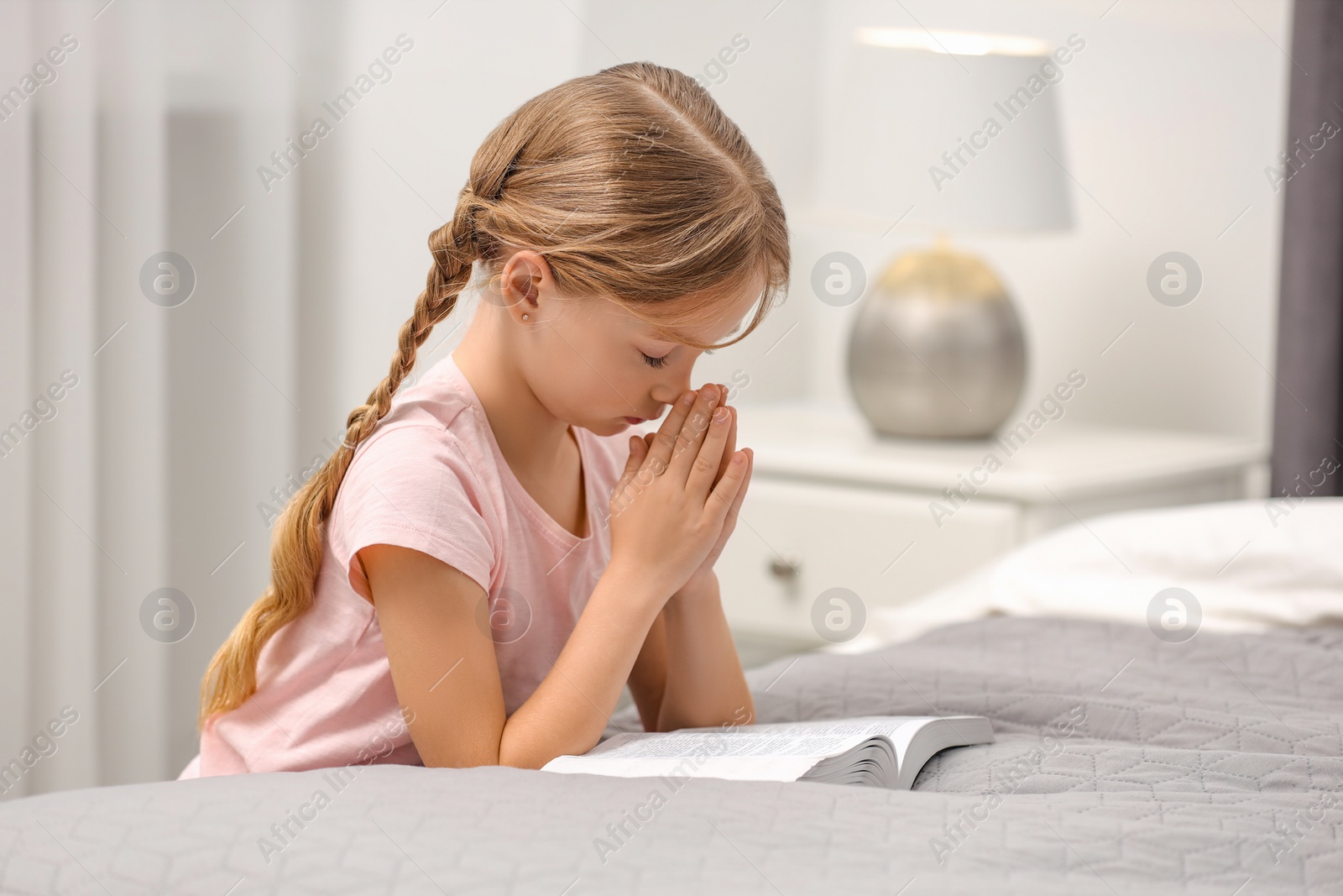 Photo of Girl holding hands clasped while praying over Bible in room