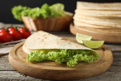 Photo of Tasty homemade tortillas, lettuce, lime and tomatoes on wooden table, closeup