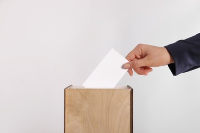 Photo of Woman putting her vote into ballot box on light grey background, closeup