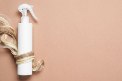 Photo of Spray bottle with thermal protection wrapped in lock of blonde hair on beige background, flat lay. Space for text