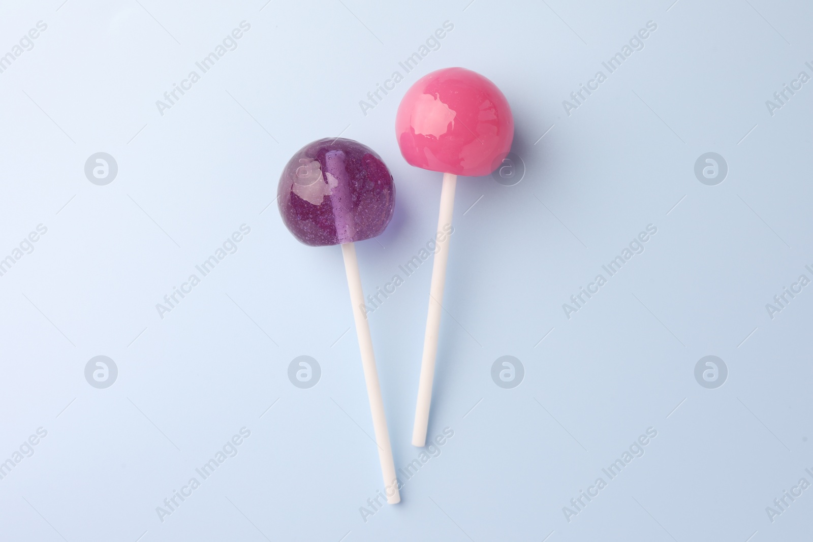 Photo of Two tasty lollipops on light blue background, flat lay