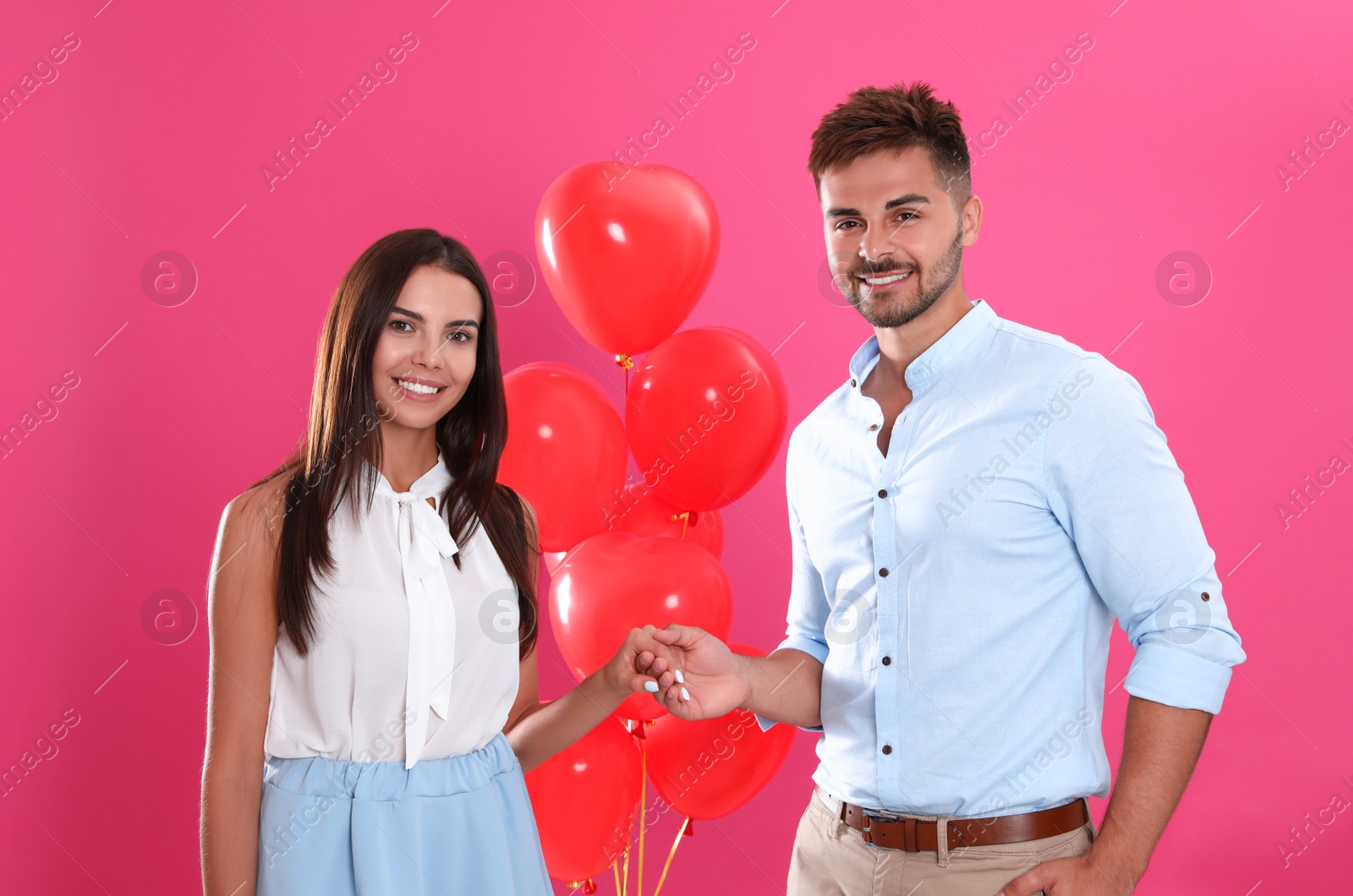 Photo of Young couple and air balloons on pink background. Celebration of Saint Valentine's Day