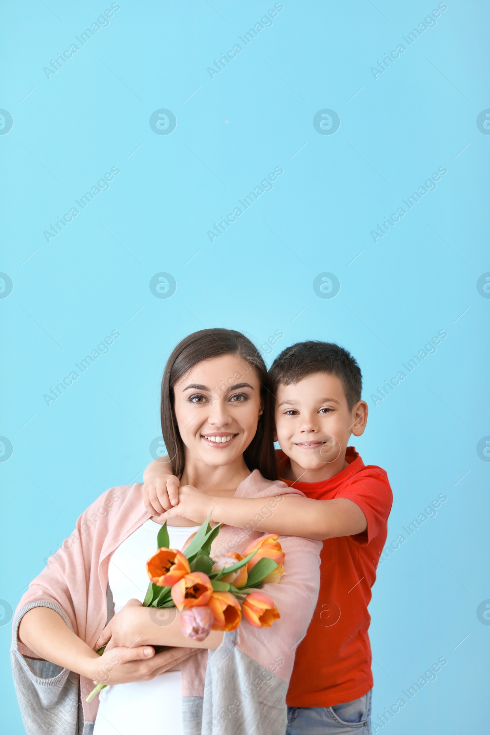 Photo of Portrait of happy woman with flowers and her son on color background. Mother's day celebration