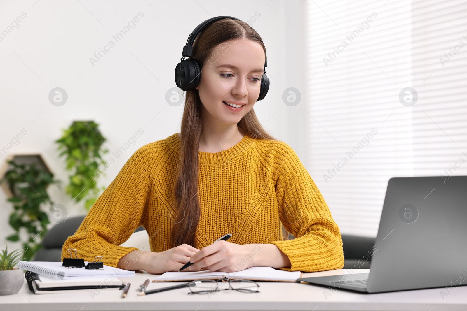 Photo of E-learning. Young woman taking notes during online lesson at white table indoors