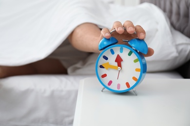 Man turning off alarm clock in bedroom