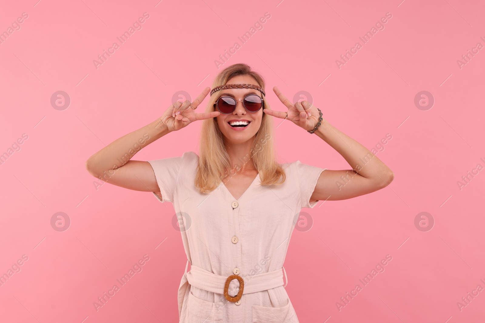 Photo of Portrait of smiling hippie woman showing peace signs on pink background