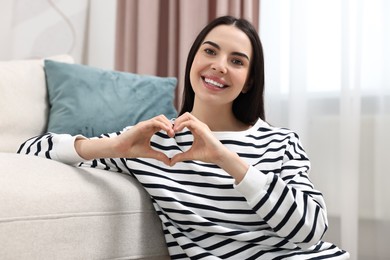 Photo of Happy young woman making heart with hands at home
