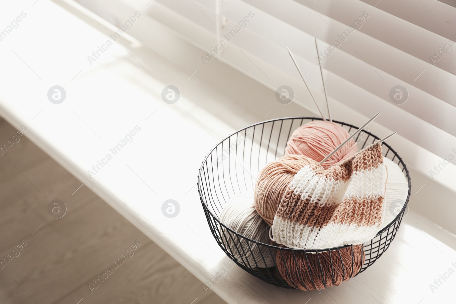 Photo of Yarn balls and knitting needles in metal basket on window sill indoors, space for text. Creative hobby