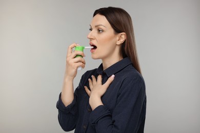 Woman using throat spray on grey background
