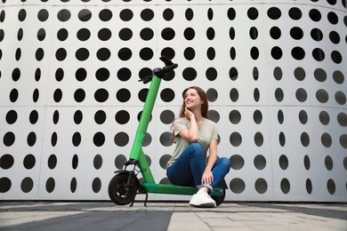 Happy woman sitting on modern electric kick scooter on city street