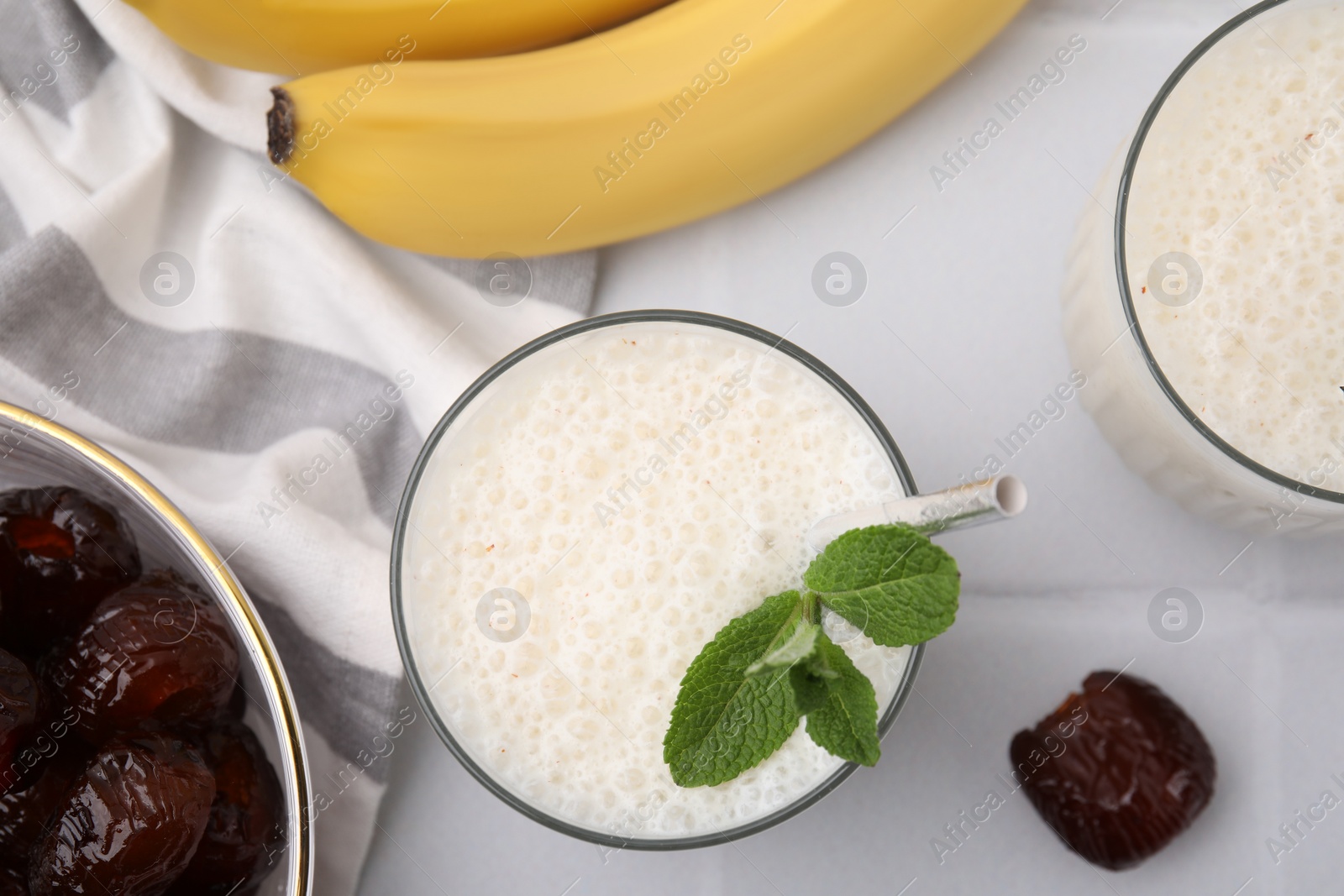 Photo of Glass of delicious date smoothie with mint, bananas and dried fruits on white table, flat lay