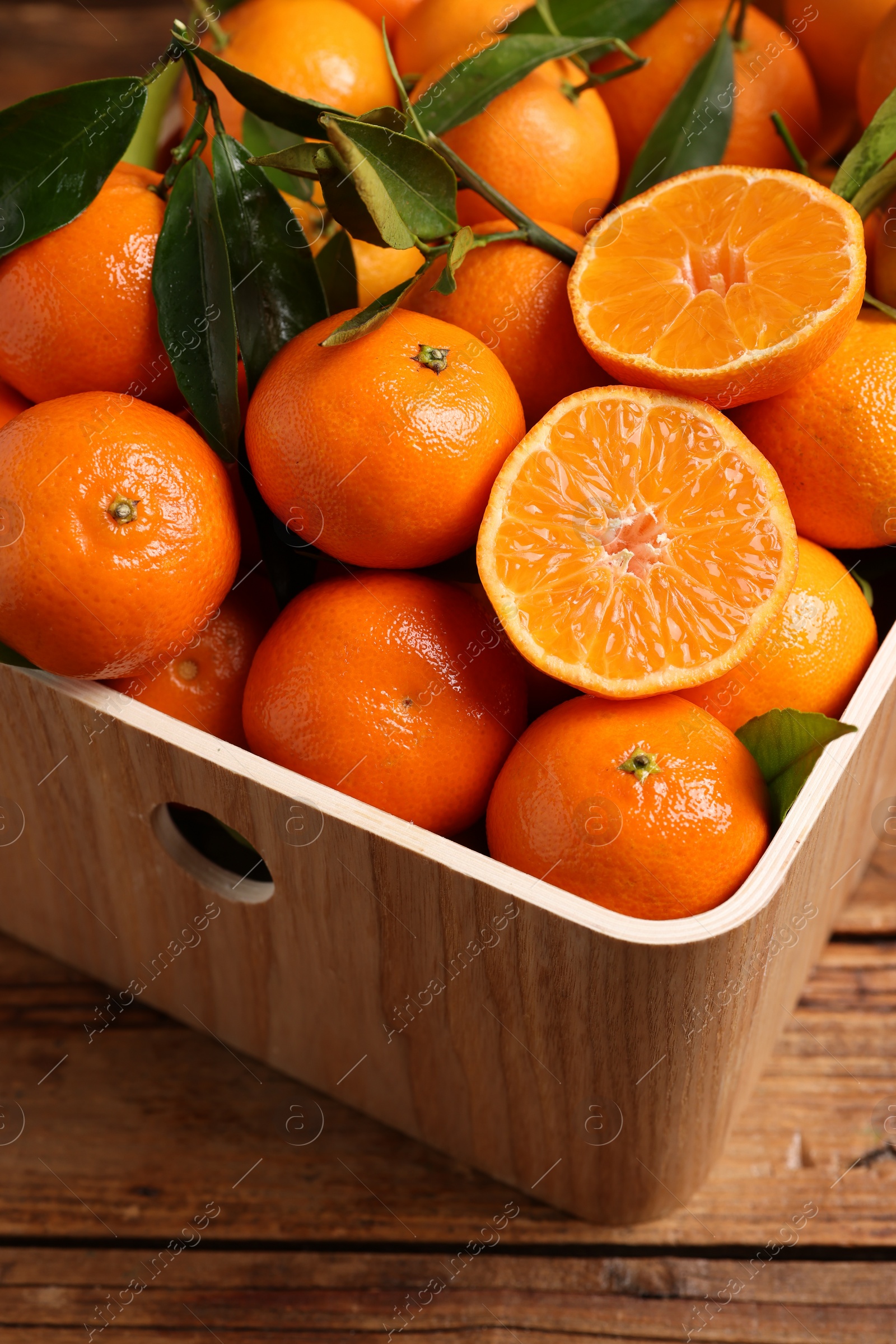 Photo of Fresh tangerines with green leaves in crate on wooden table, closeup